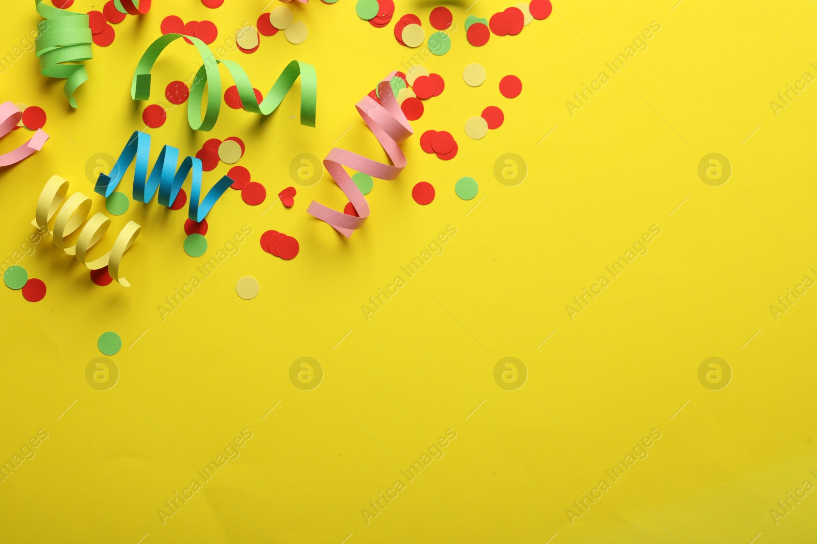 Photo of Colorful serpentine streamers and confetti on yellow background, flat lay. Space for text