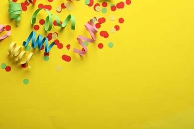 Photo of Colorful serpentine streamers and confetti on yellow background, flat lay. Space for text