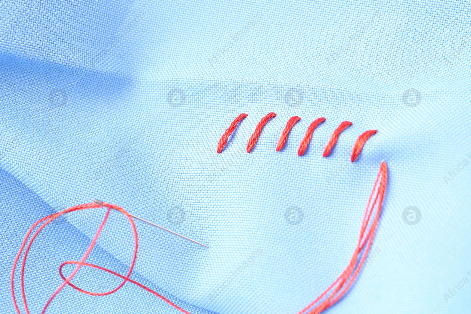 Photo of Sewing needle with thread and stitches on light blue cloth, closeup