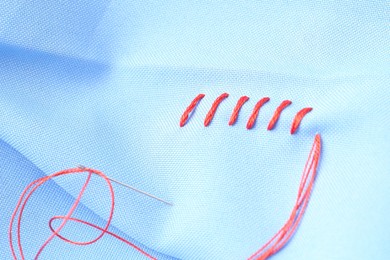 Photo of Sewing needle with thread and stitches on light blue cloth, closeup