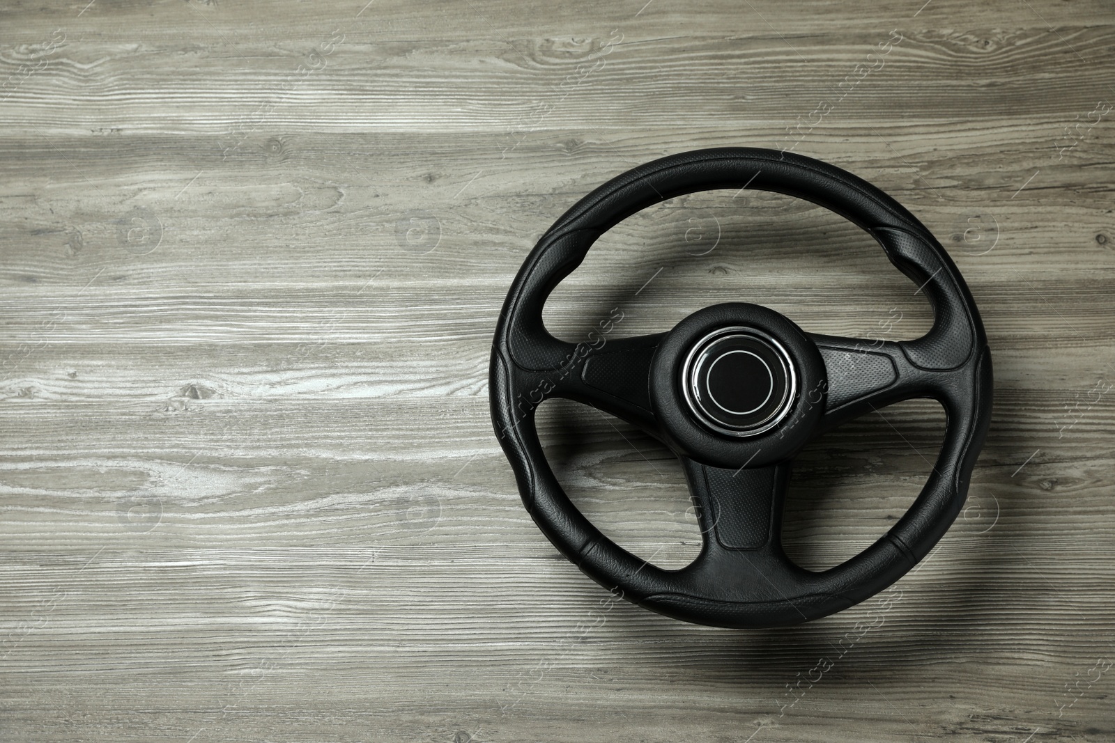 Photo of New black steering wheel on grey wooden table, top view. Space for text