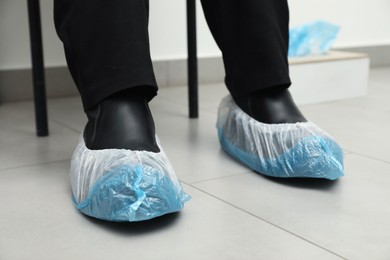 Woman wearing blue shoe covers onto her boots indoors, closeup