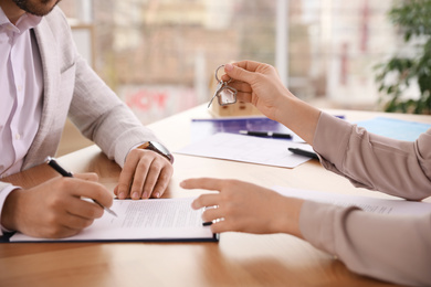 Photo of Real estate agent giving key with trinket to client in office, closeup