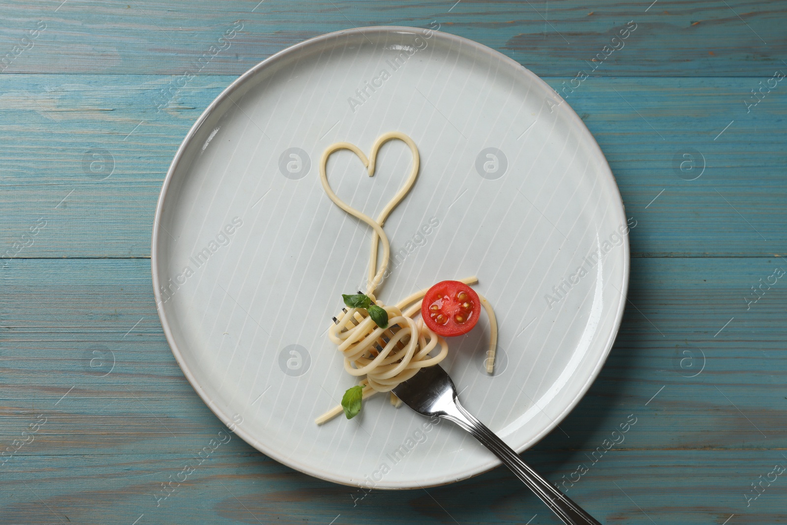 Photo of Heart made of tasty spaghetti, fork and tomato on light blue wooden table, top view