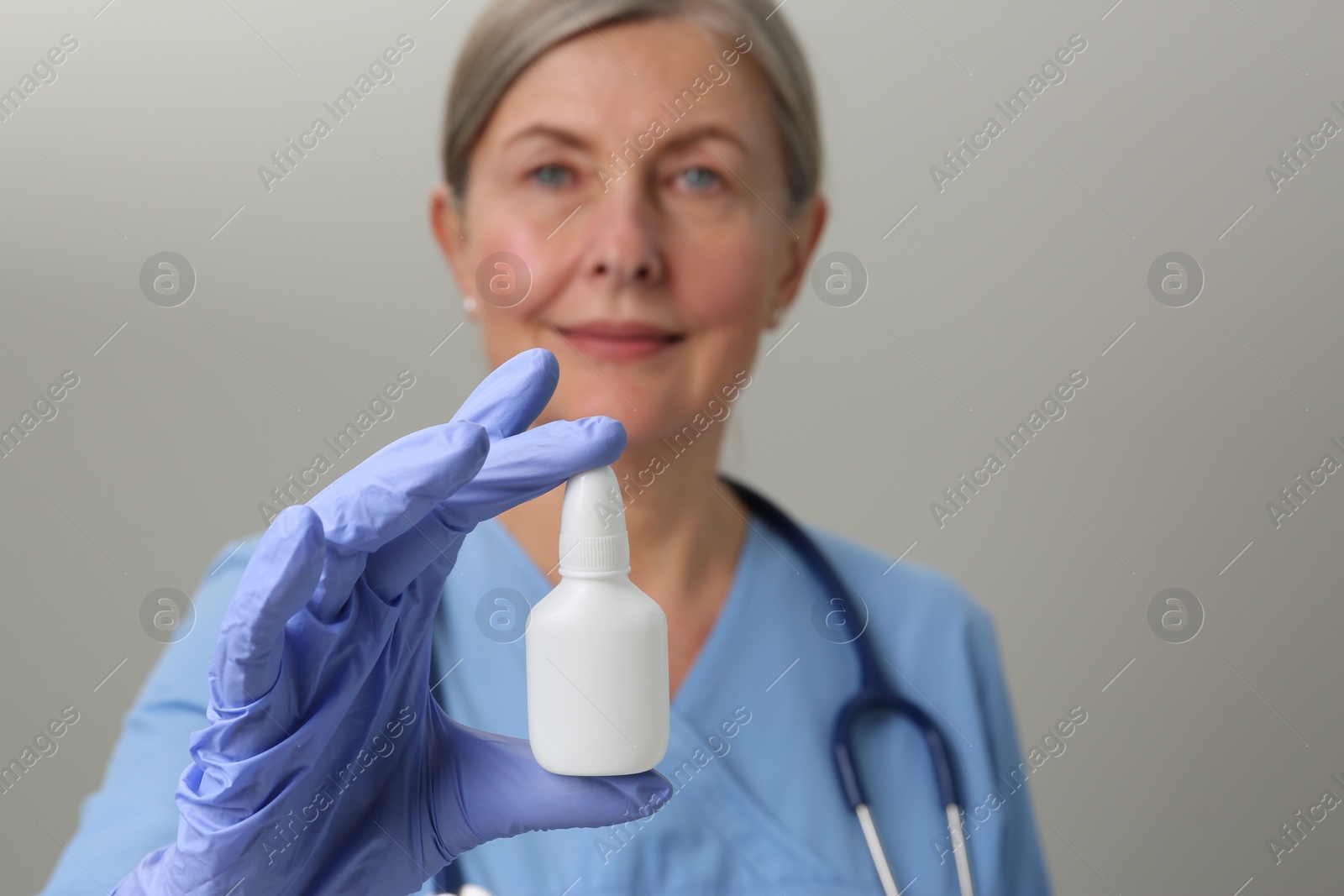 Photo of Woman holding nasal spray against light grey background, focus on bottle