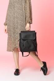 Woman in dress and stylish shoes holding backpack on color background