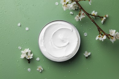 Photo of Flat lay composition with jar of face cream and flowers on wet green surface