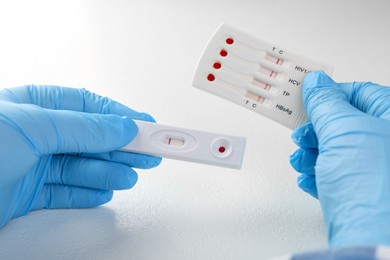 Photo of Doctor holding two disposable express tests at white table, closeup