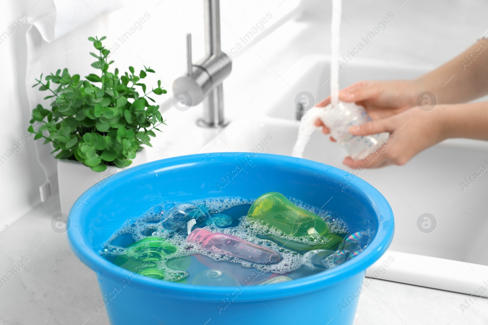 Photo of Woman washing baby bottle in kitchen, focus on basin with children's dishes