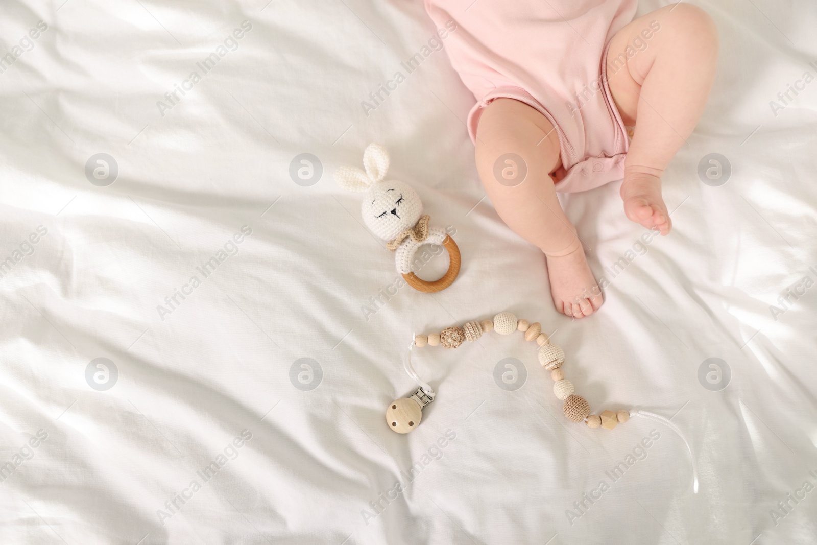 Photo of Cute baby with rattle and teether toys on sheets, top view. Space for text