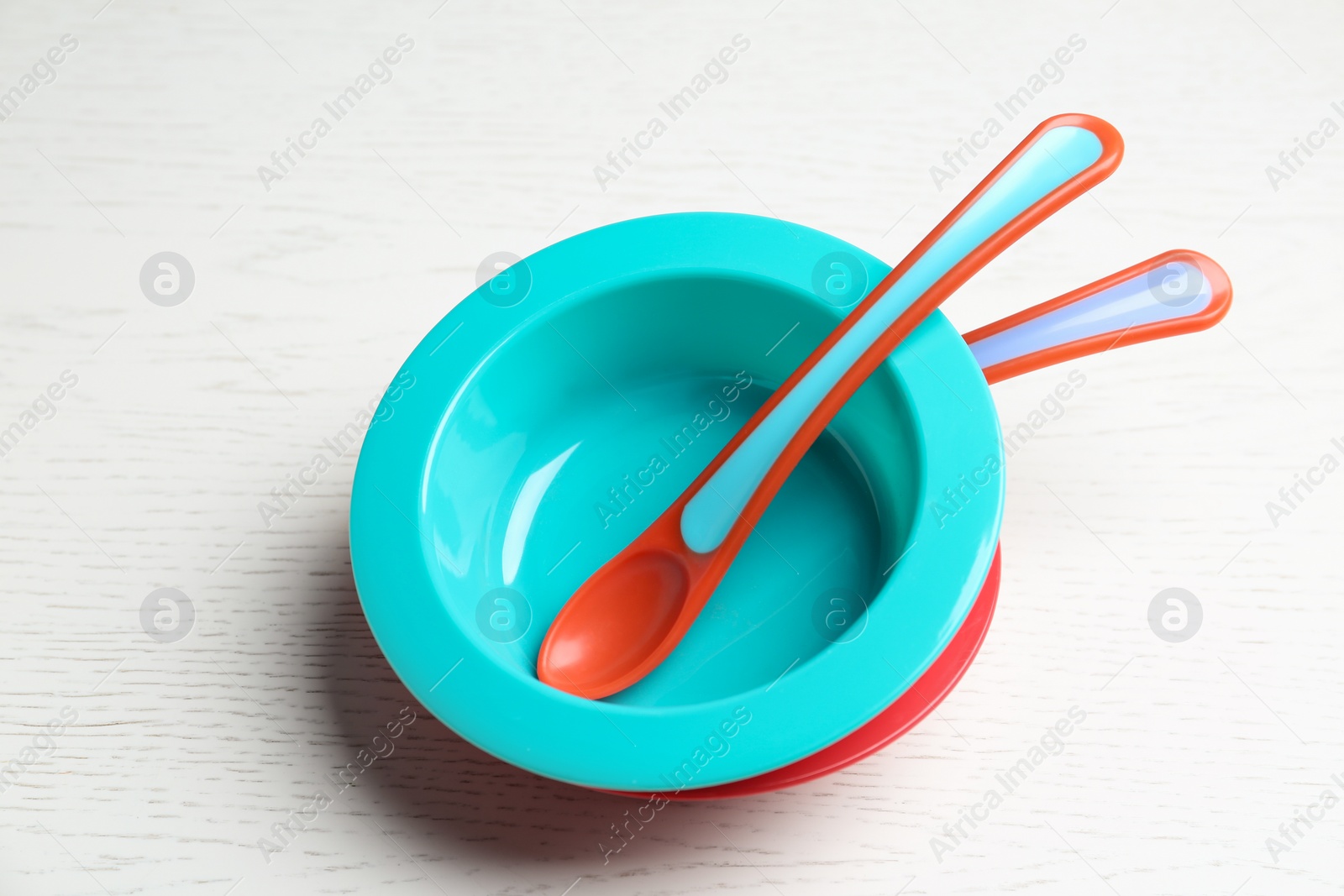 Photo of Plastic bowls with spoons on white wooden table. Serving baby food