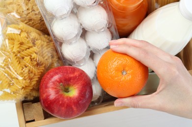 Humanitarian aid. Woman with food products for donation at white wooden table, top view