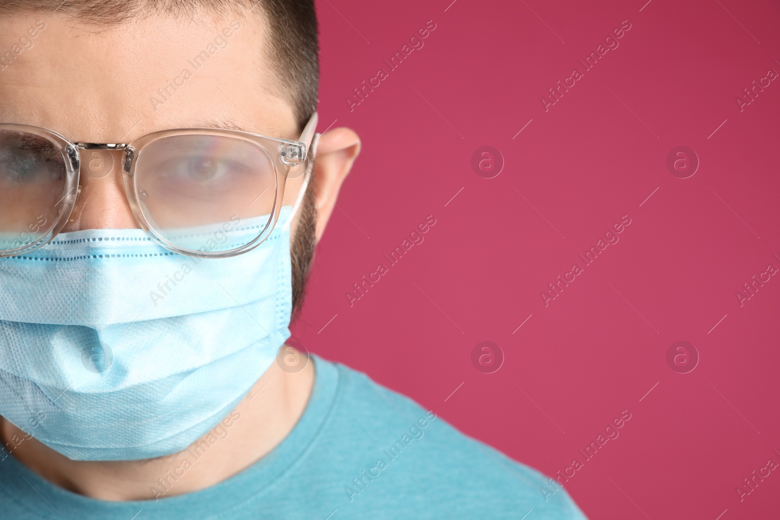 Photo of Man with foggy glasses caused by wearing disposable mask on pink background, space for text. Protective measure during coronavirus pandemic