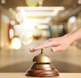 Woman ringing hotel service bell on blurred background, closeup