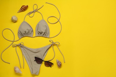 Photo of Stylish beige bikini, sunglasses and seashells on yellow background, flat lay. Space for text