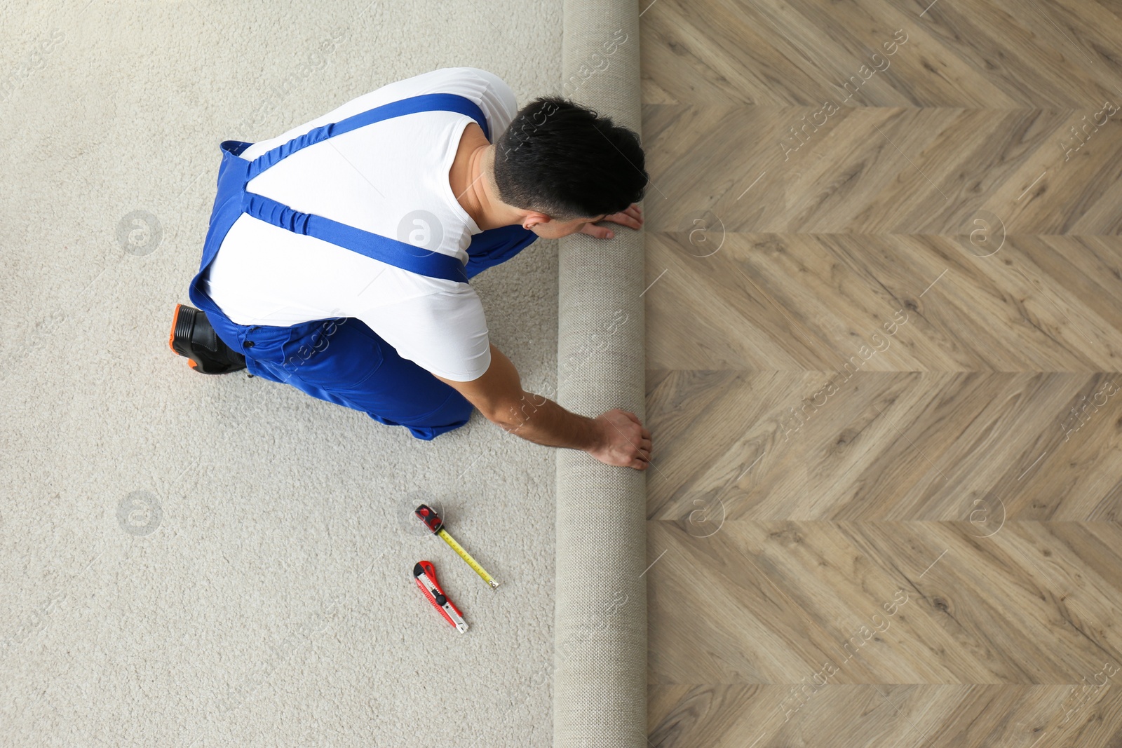 Photo of Worker rolling out new carpet indoors, above view