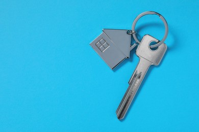 Photo of Metallic key with keychain in shape of house on light blue background, top view. Space for text