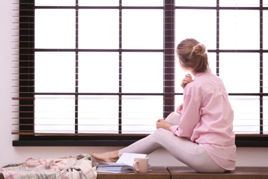 Young woman relaxing near window with blinds at home. Space for text