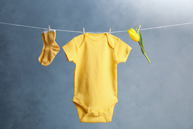 Photo of Child's bodysuit, pair of socks and flower hanging on laundry line against dark background