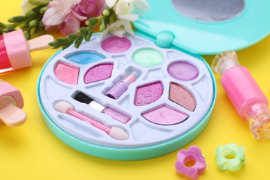 Photo of Decorative cosmetics for kids. Eye shadow palette, lipsticks, accessories and flowers on yellow background, closeup