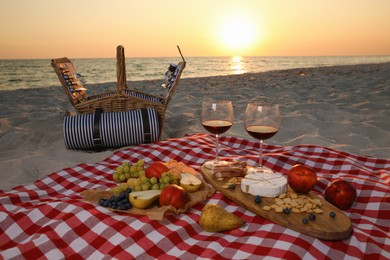 Blanket with wine and snacks for picnic near basket on sandy beach
