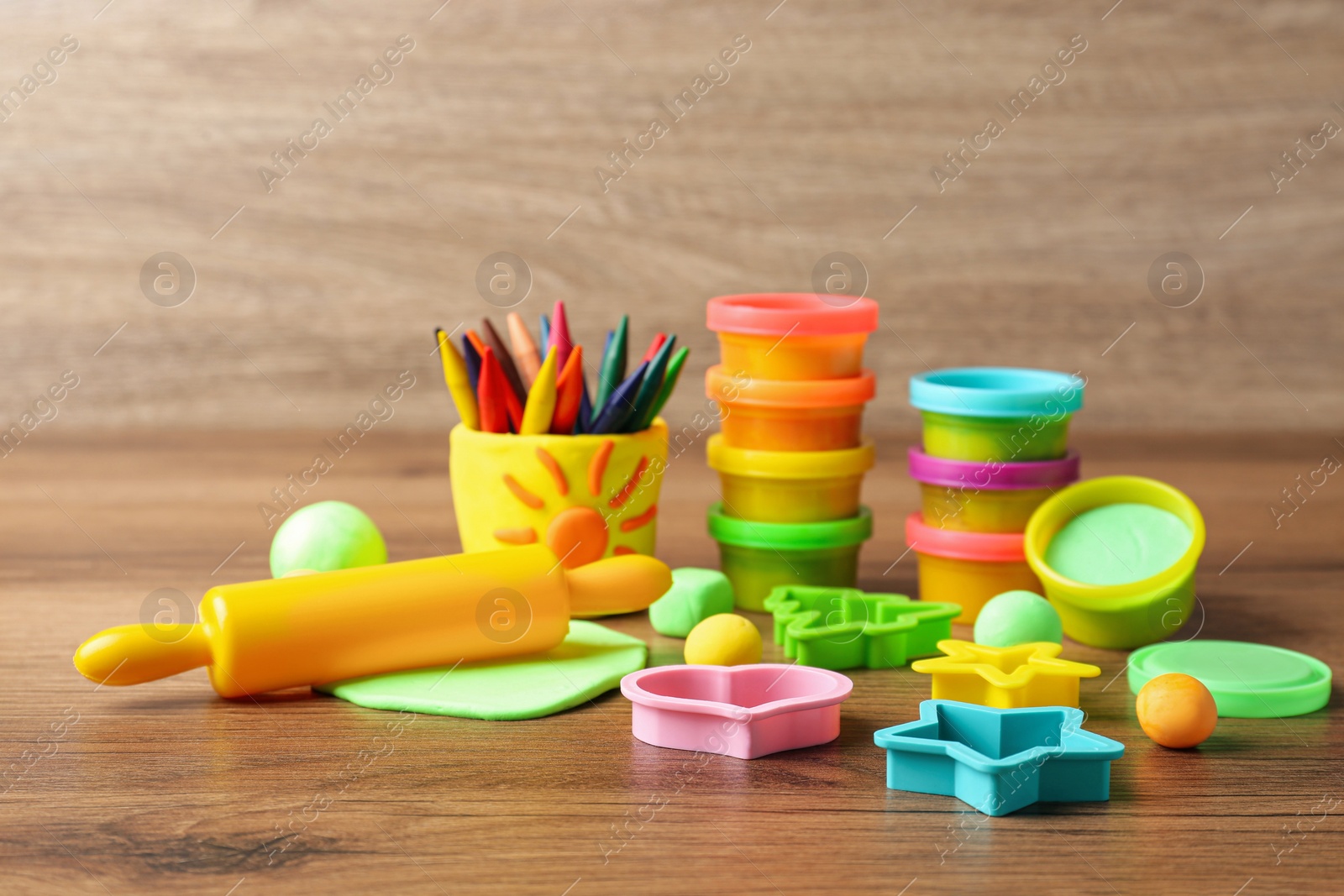 Photo of Set of bright play dough with tools and colorful pencils on wooden table