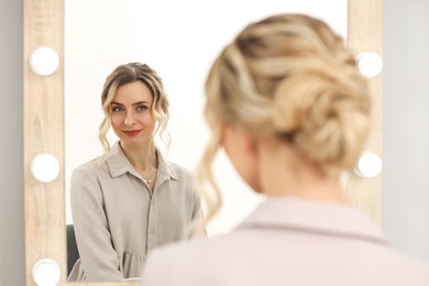 Woman with beautiful hair style looking at mirror indoors