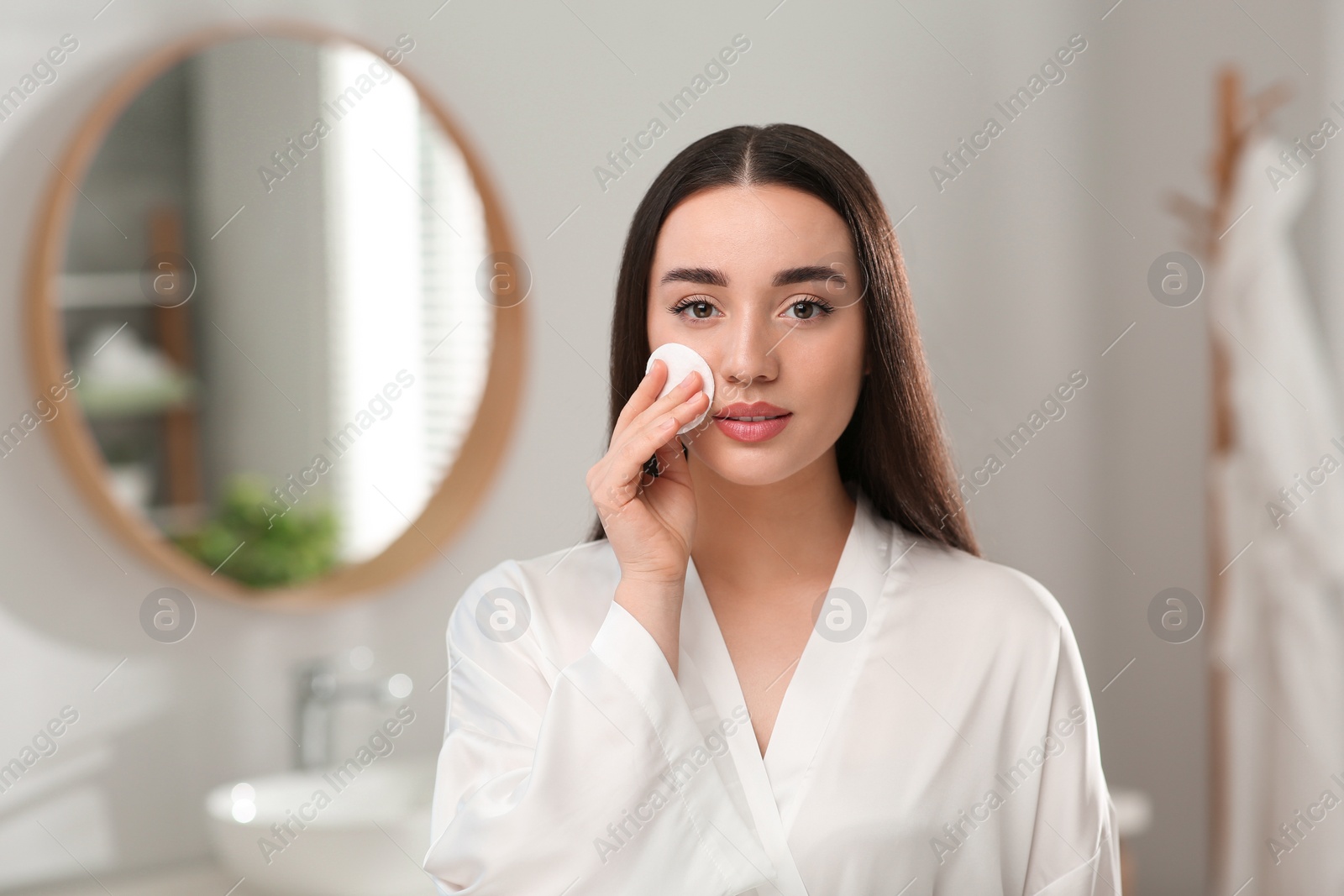 Photo of Beautiful woman removing makeup with cotton pad indoors