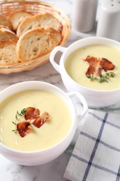 Photo of Tasty potato soup with bacon and rosemary in bowls on white marble table