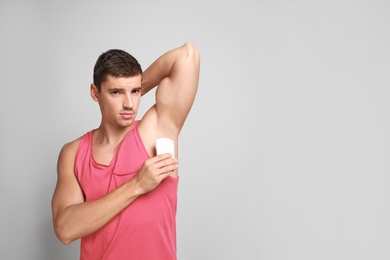 Photo of Young man applying deodorant to armpit on light background. Space for text