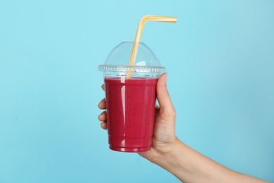 Woman holding plastic cup with delicious smoothie on color background