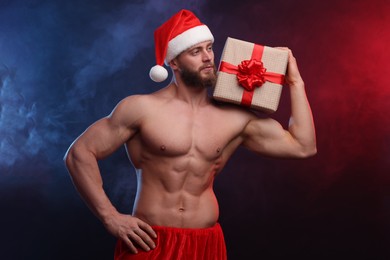 Attractive young man with muscular body holding Christmas gift box on color background