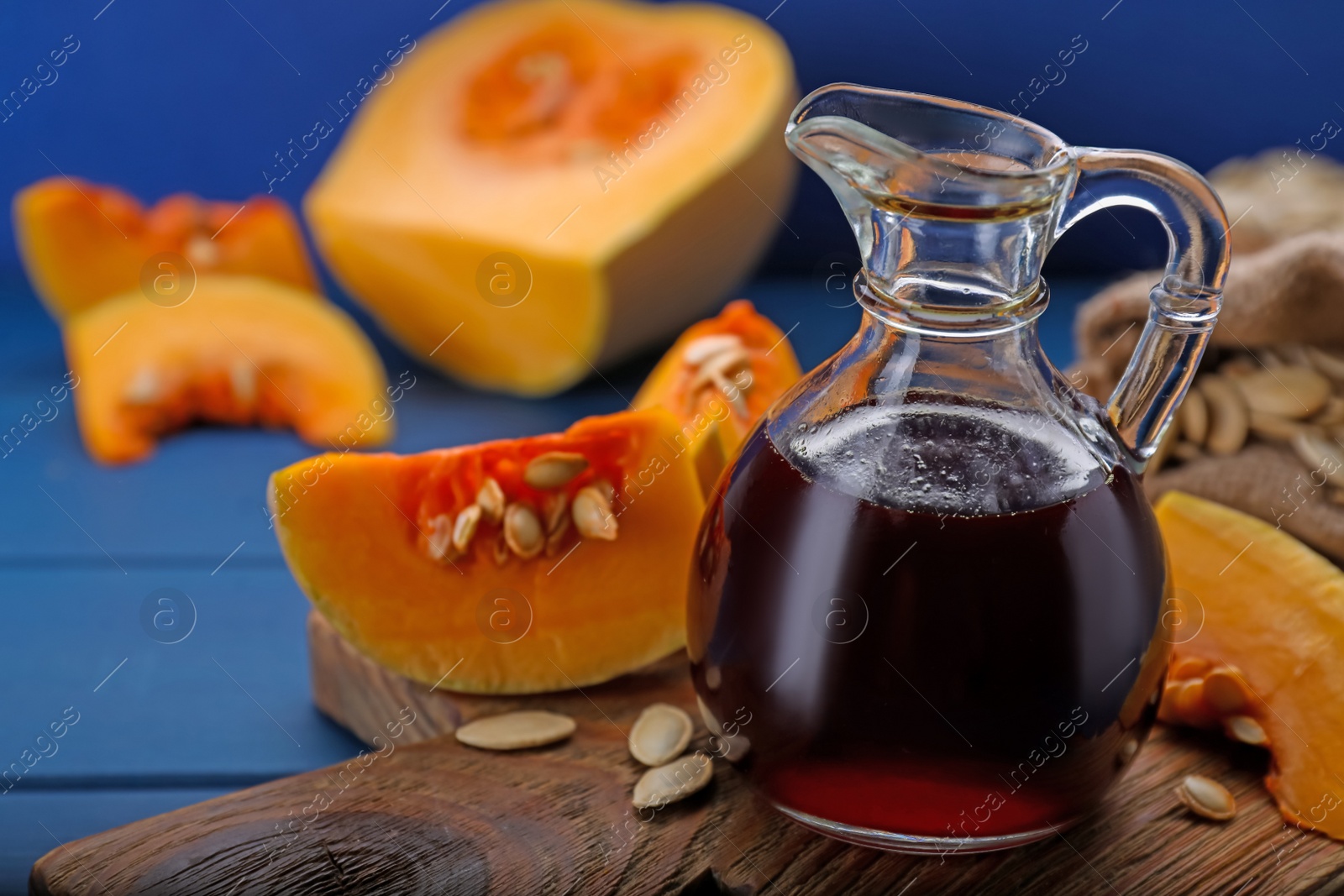 Photo of Fresh pumpkin seed oil in glass jug on blue wooden table