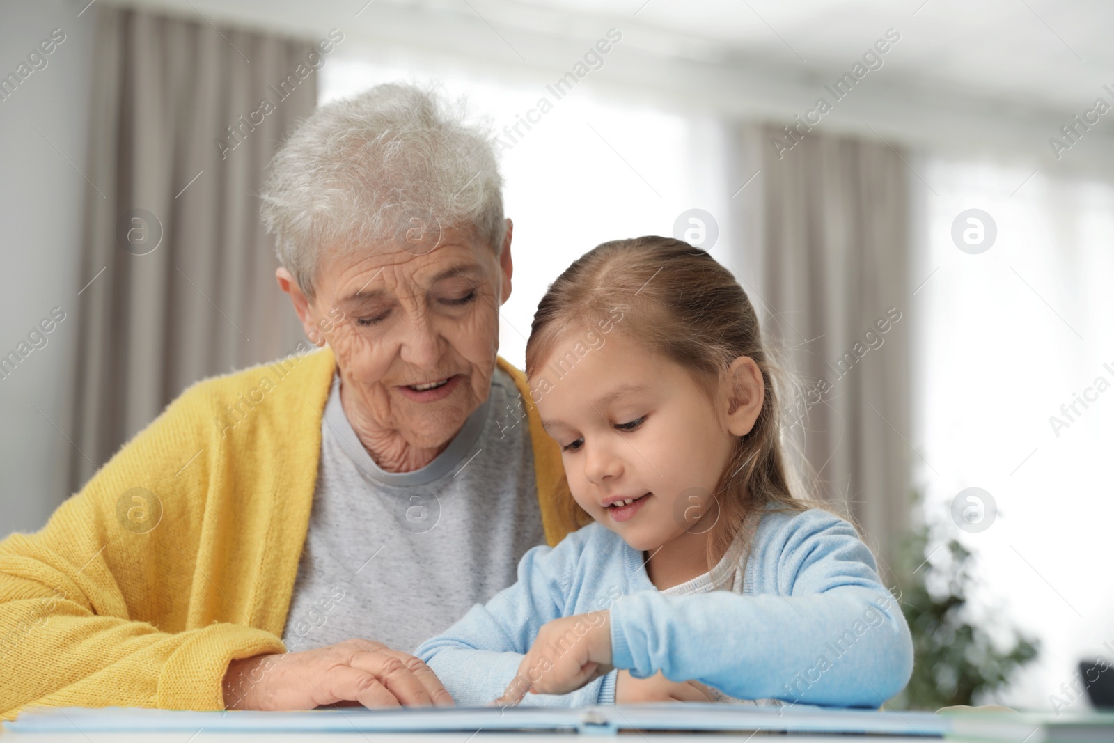 Photo of Cute girl and her grandmother reading book at home