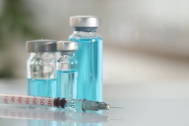 Photo of Glass vials with light blue medication and syringe on white table, closeup. Space for text