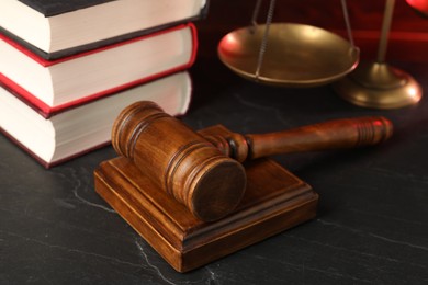 Photo of Wooden gavel, scales and stack of books on dark textured table, closeup