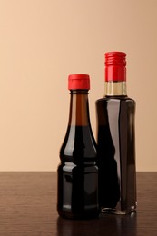 Photo of Bottles with soy sauce on wooden table against beige background
