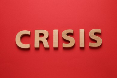 Photo of Word Crisis made of wooden letters on red background, flat lay