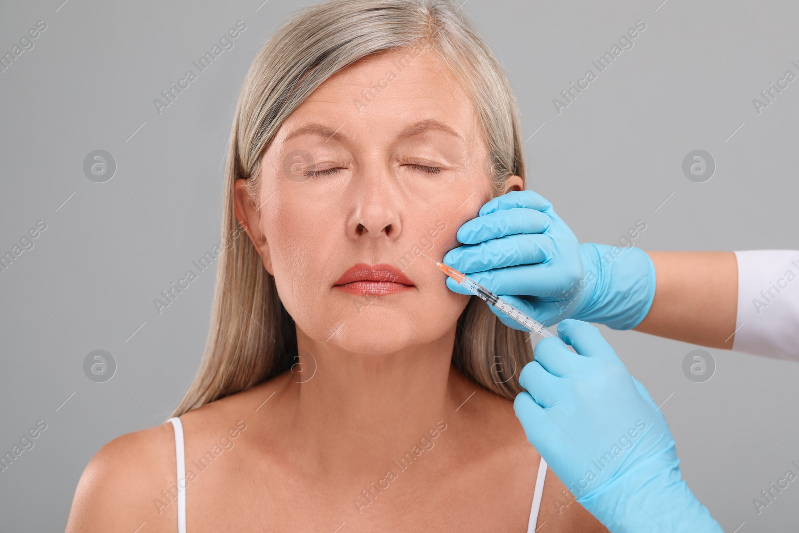 Photo of Doctor giving facial injection to senior woman on light grey background, closeup. Cosmetic surgery