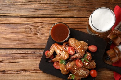 Glass of beer, delicious baked chicken wings and sauce on wooden table, flat lay. Space for text