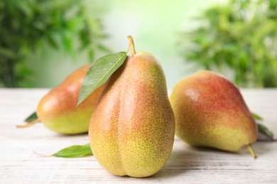 Photo of Ripe juicy pears on white wooden table against blurred background