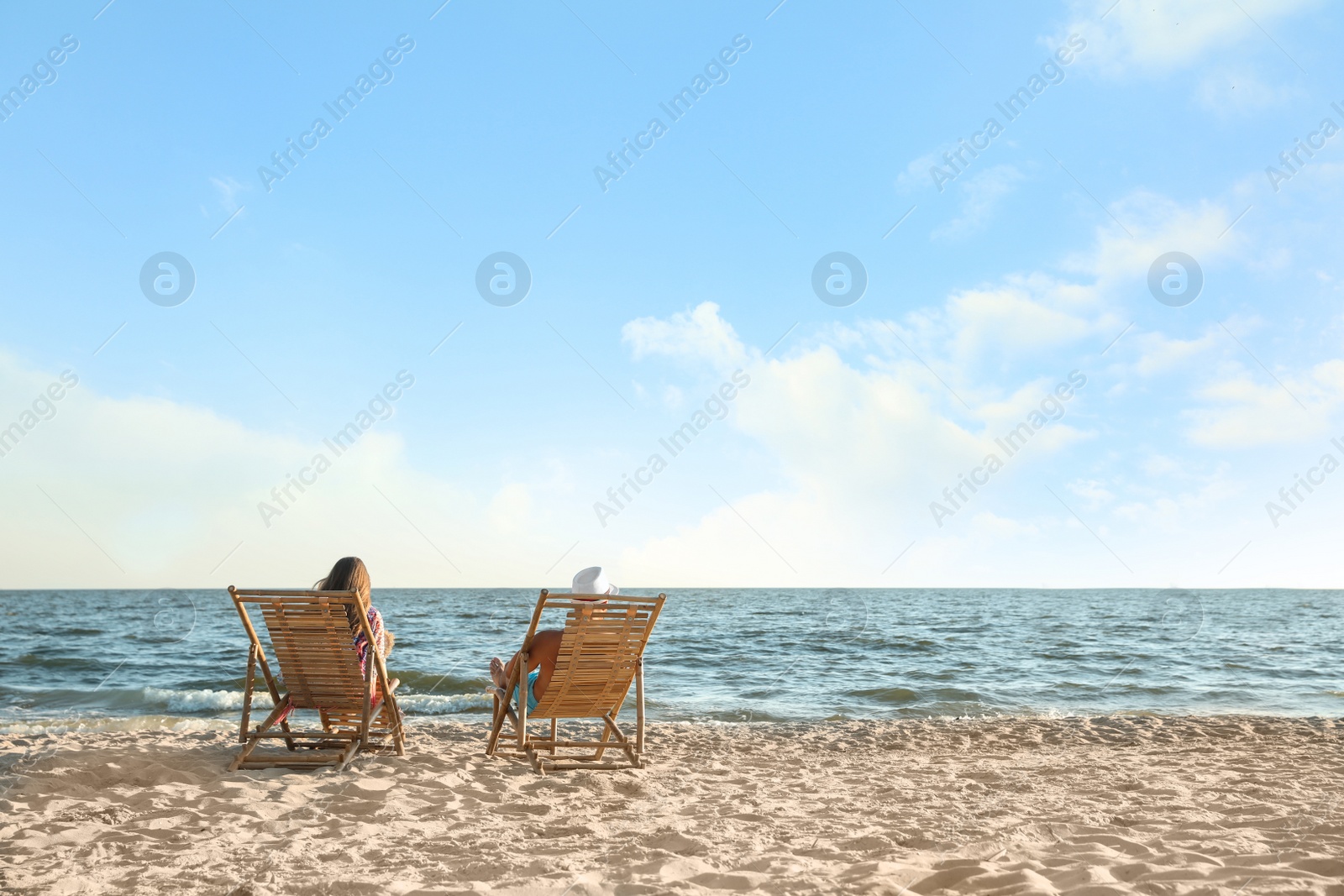 Photo of Young couple relaxing in deck chairs on beach near sea