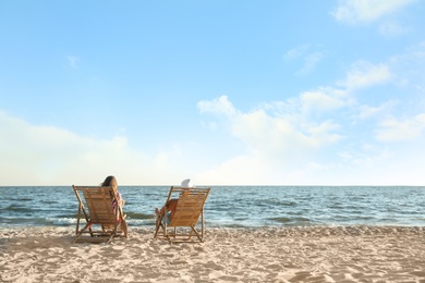 Young couple relaxing in deck chairs on beach near sea