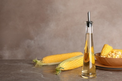 Bottle of corn oil and fresh cobs on table against color wall