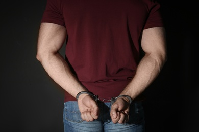 Photo of Male criminal in handcuffs near black wall, closeup