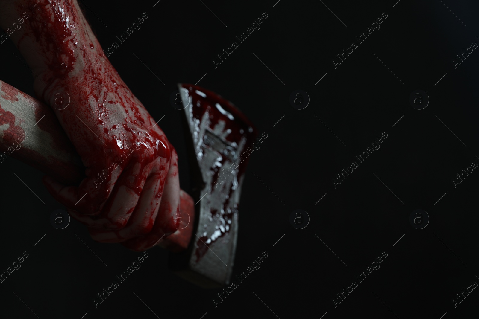 Photo of Man holding bloody axe on black background, closeup. Space for text