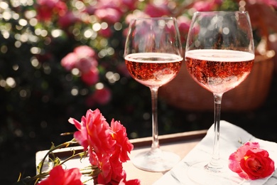 Glasses of rose wine on table in blooming garden, space for text