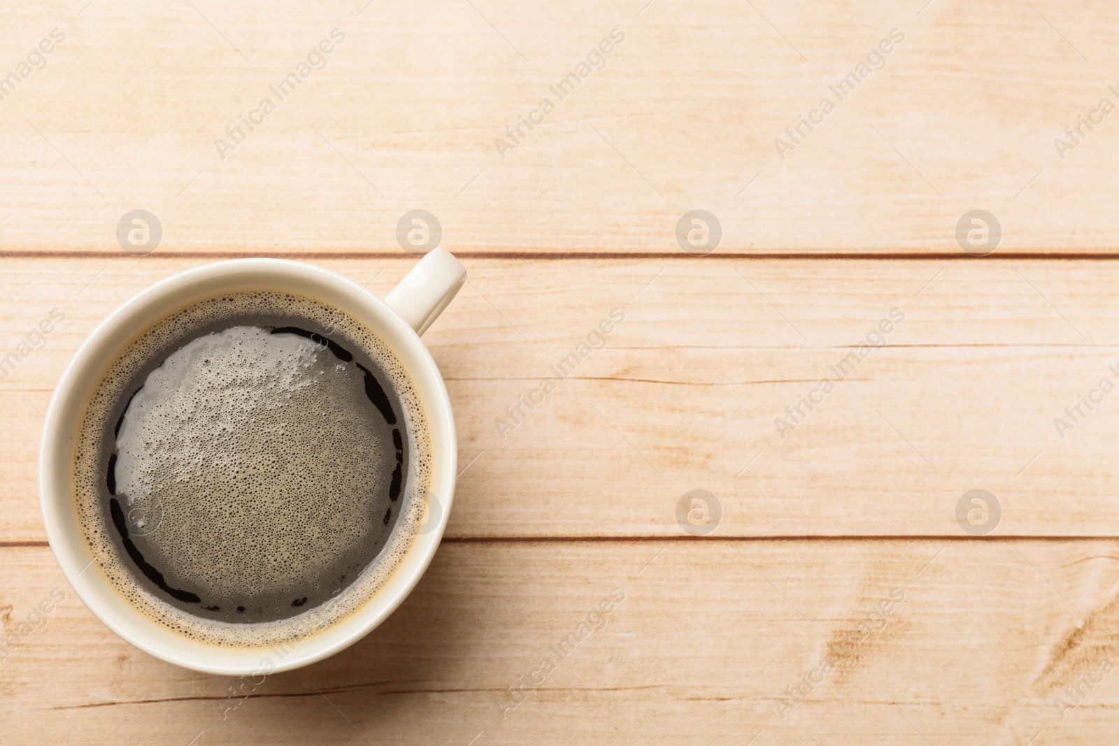 Photo of Cup of aromatic coffee on light wooden table, top view. Space for text