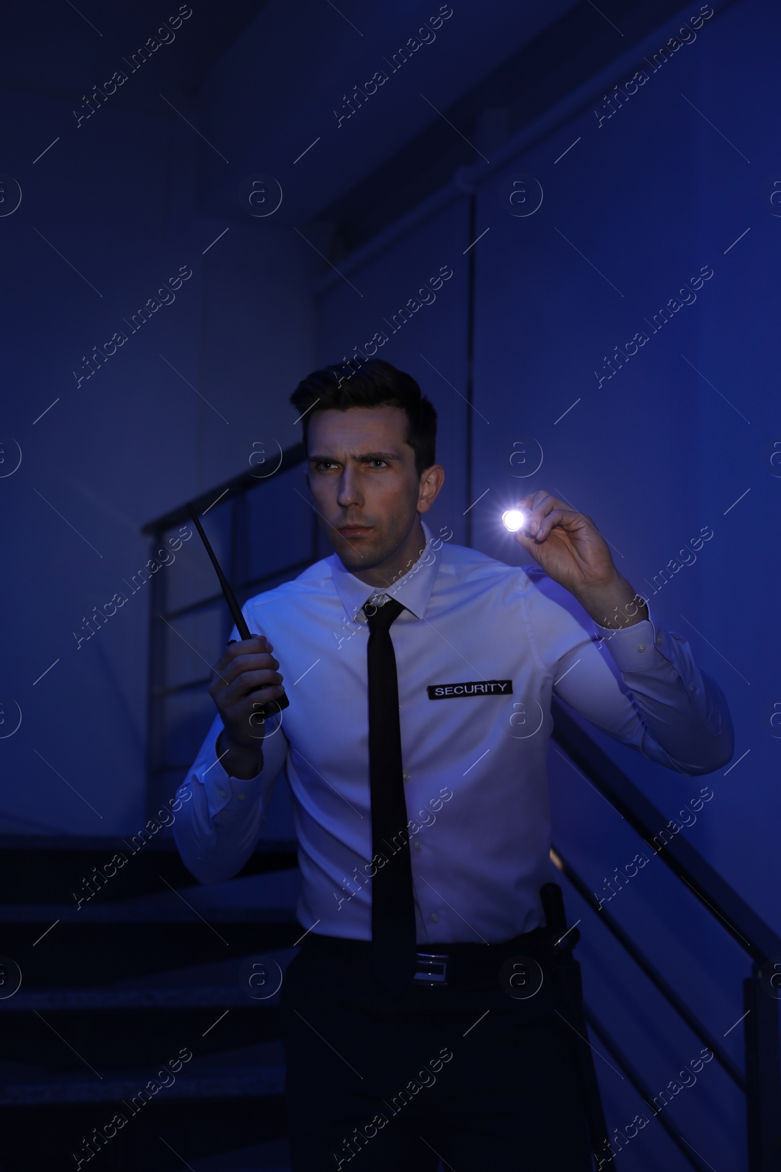 Photo of Male security guard with flashlight and portable radio transmitter in dark room