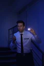 Photo of Male security guard with flashlight and portable radio transmitter in dark room